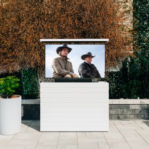 An outdoor hidden TV lift cabinet cladded in white shiplap, on a backyard patio with outdoor furniture.