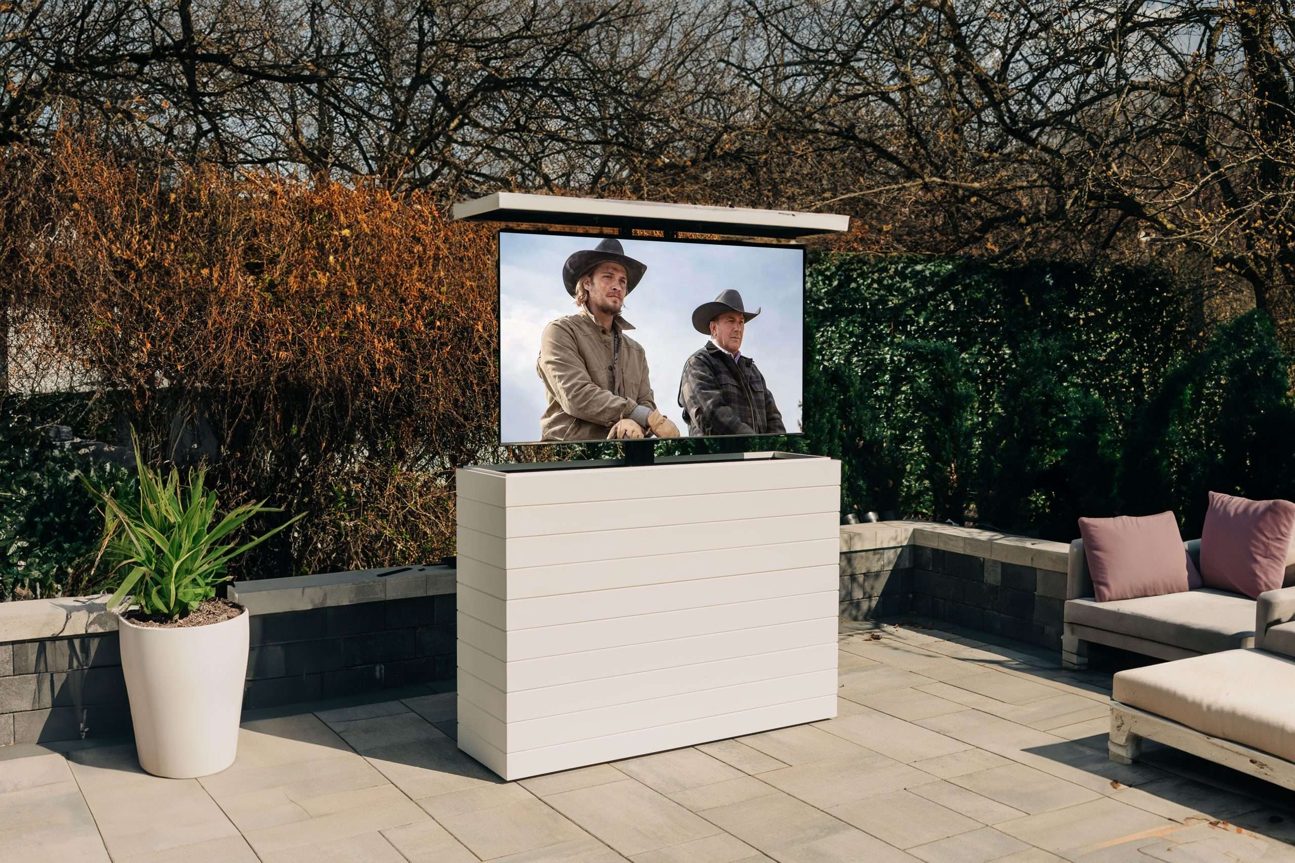 A white shiplap hidden tv lift cabinet is shown on a backyard patio.